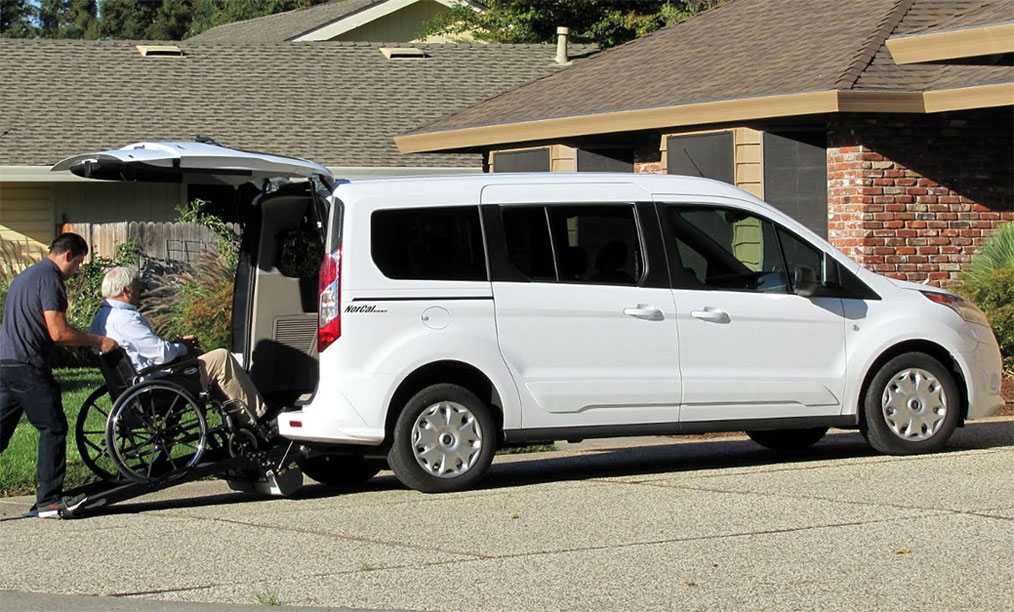 A person in a wheelchair boarding a Ford Transit from the back hatch.